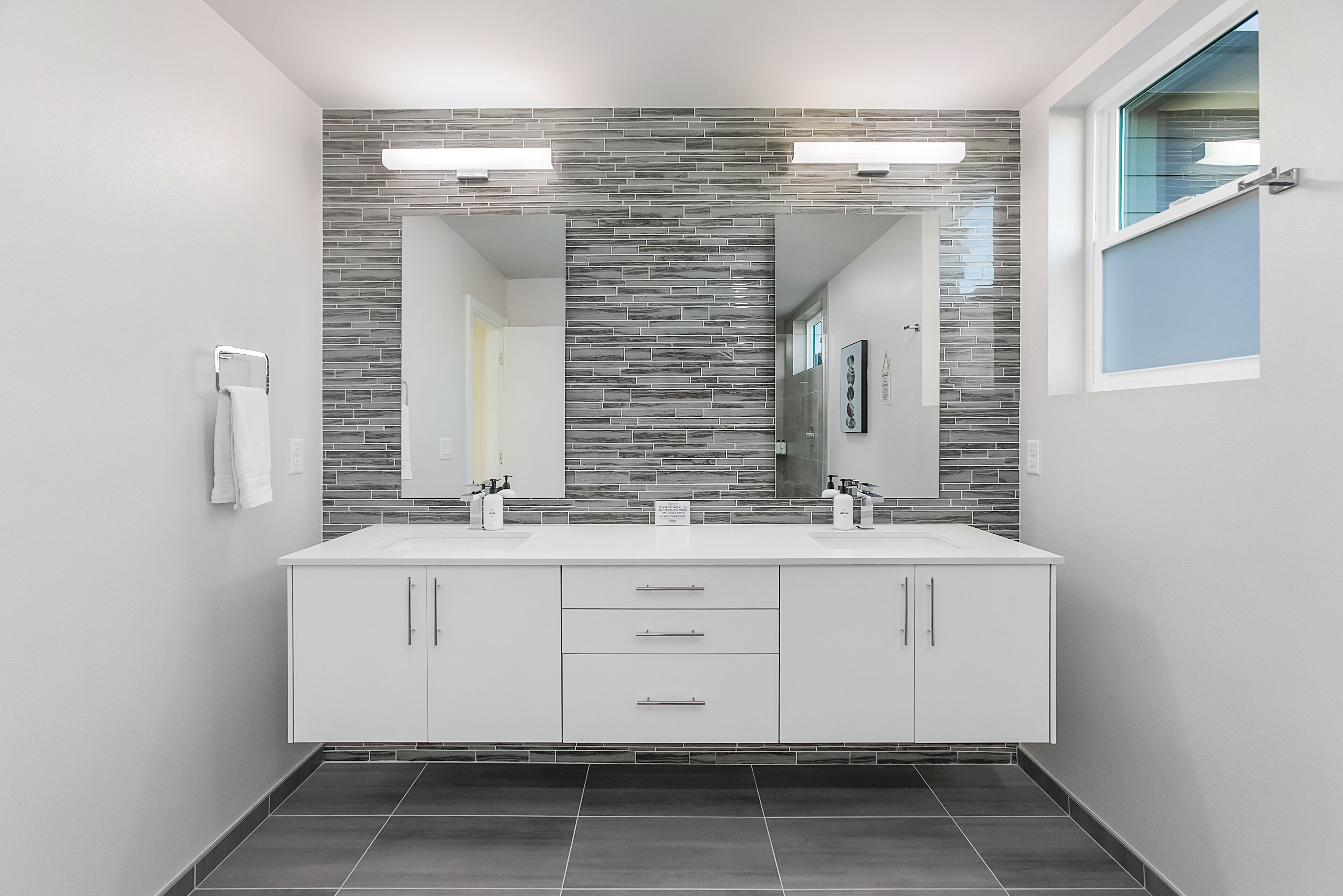 A modern bathroom with a double sink vanity, a large mirror, and a tiled backsplash.