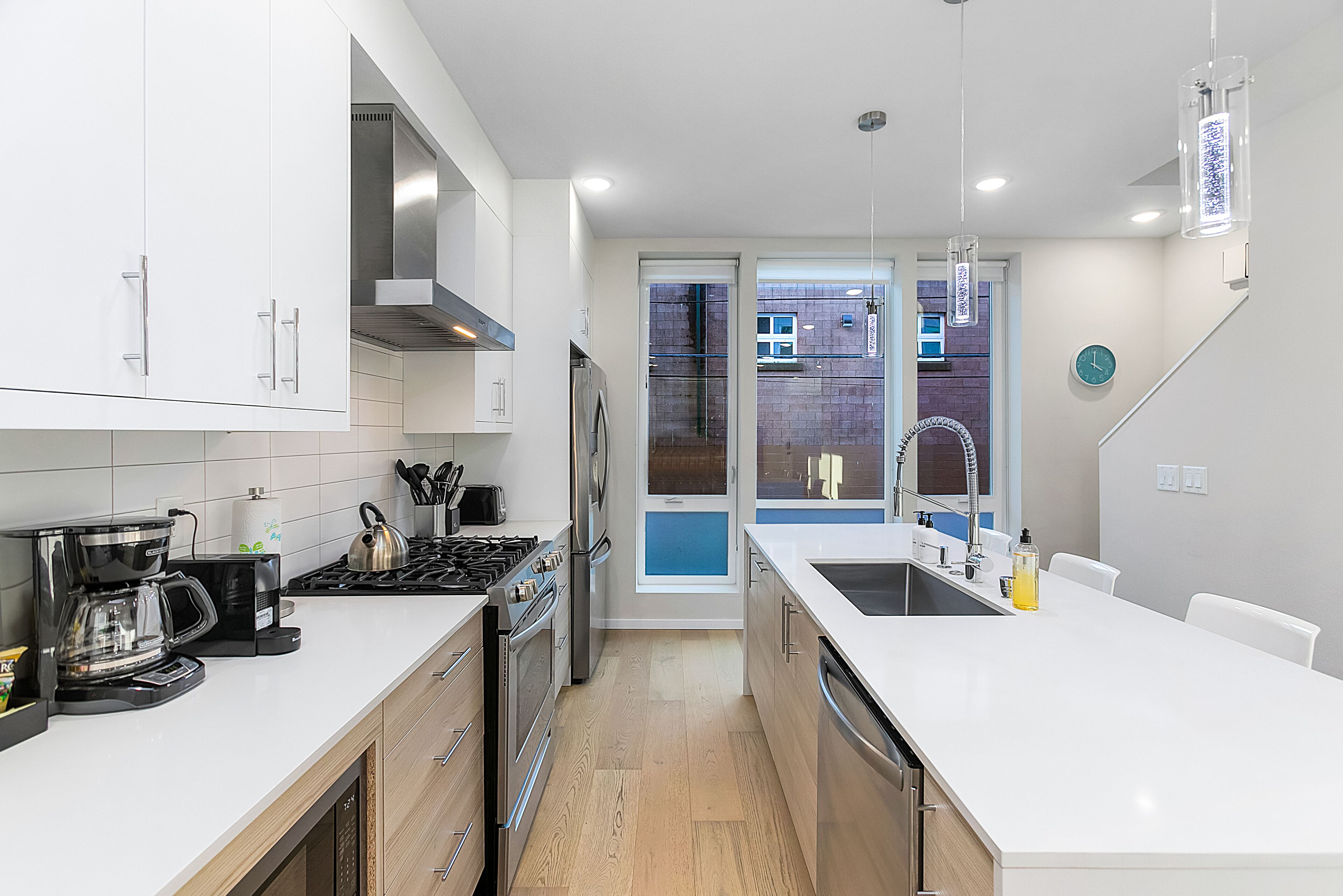 A modern kitchen with white cabinets, stainless steel appliances, and a wooden floor.