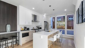 Une cuisine moderne avec des meubles blancs, un îlot central doté de tabourets, des appareils en acier inoxydable et un éclairage suspendu.