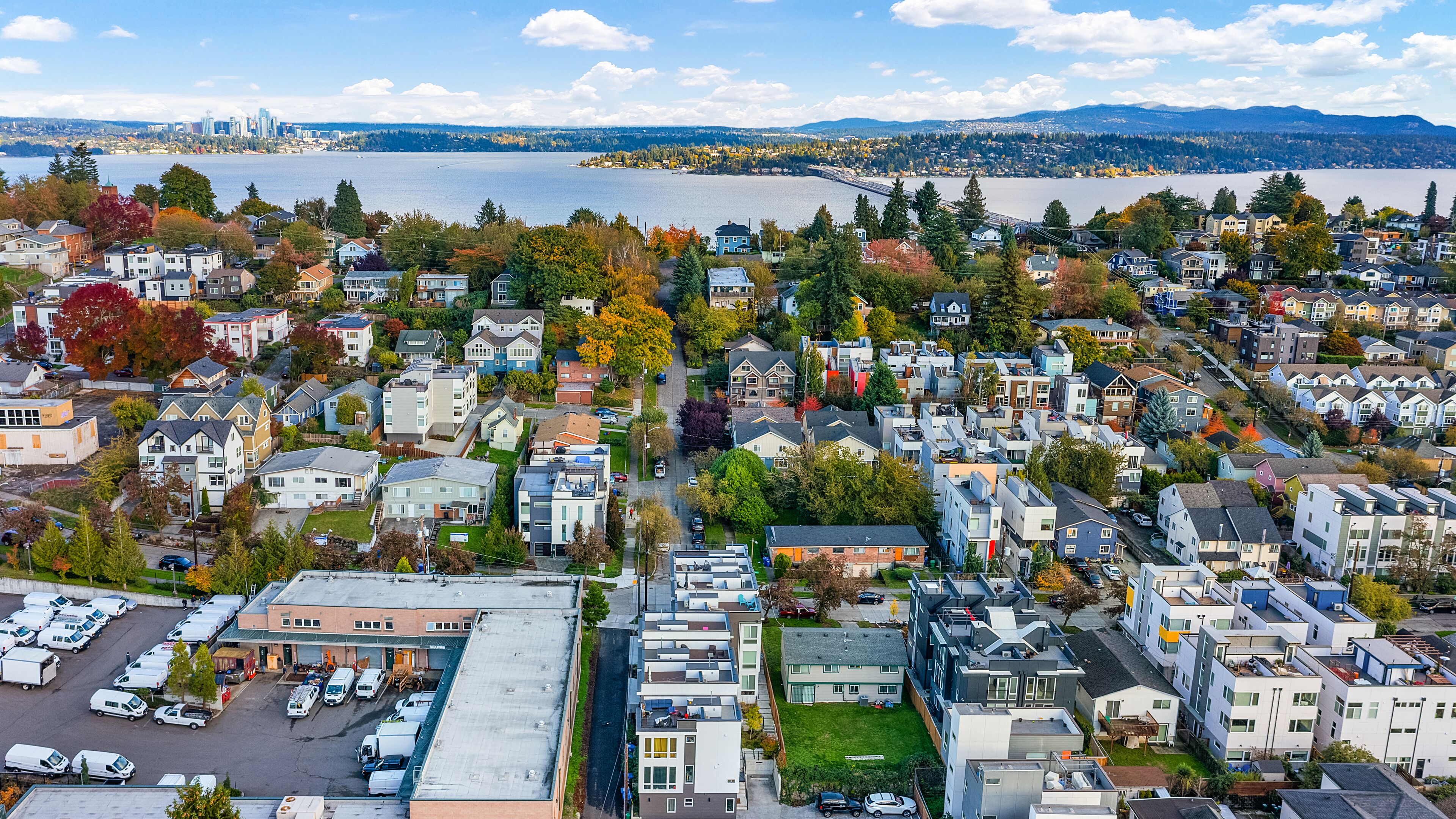 An aerial view of a residential area with houses, a parking lot, and a body of water in the background.