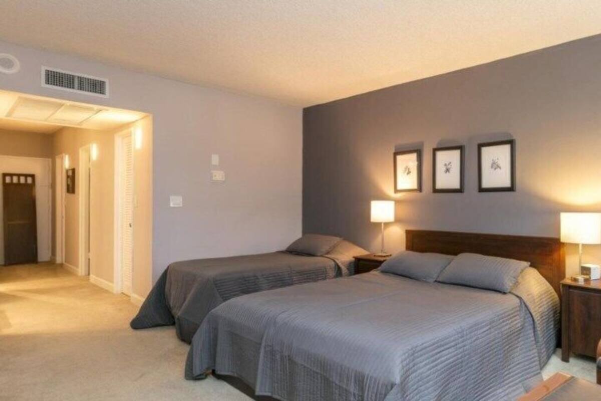 A bedroom with two beds, a chair, and a nightstand with lamps.