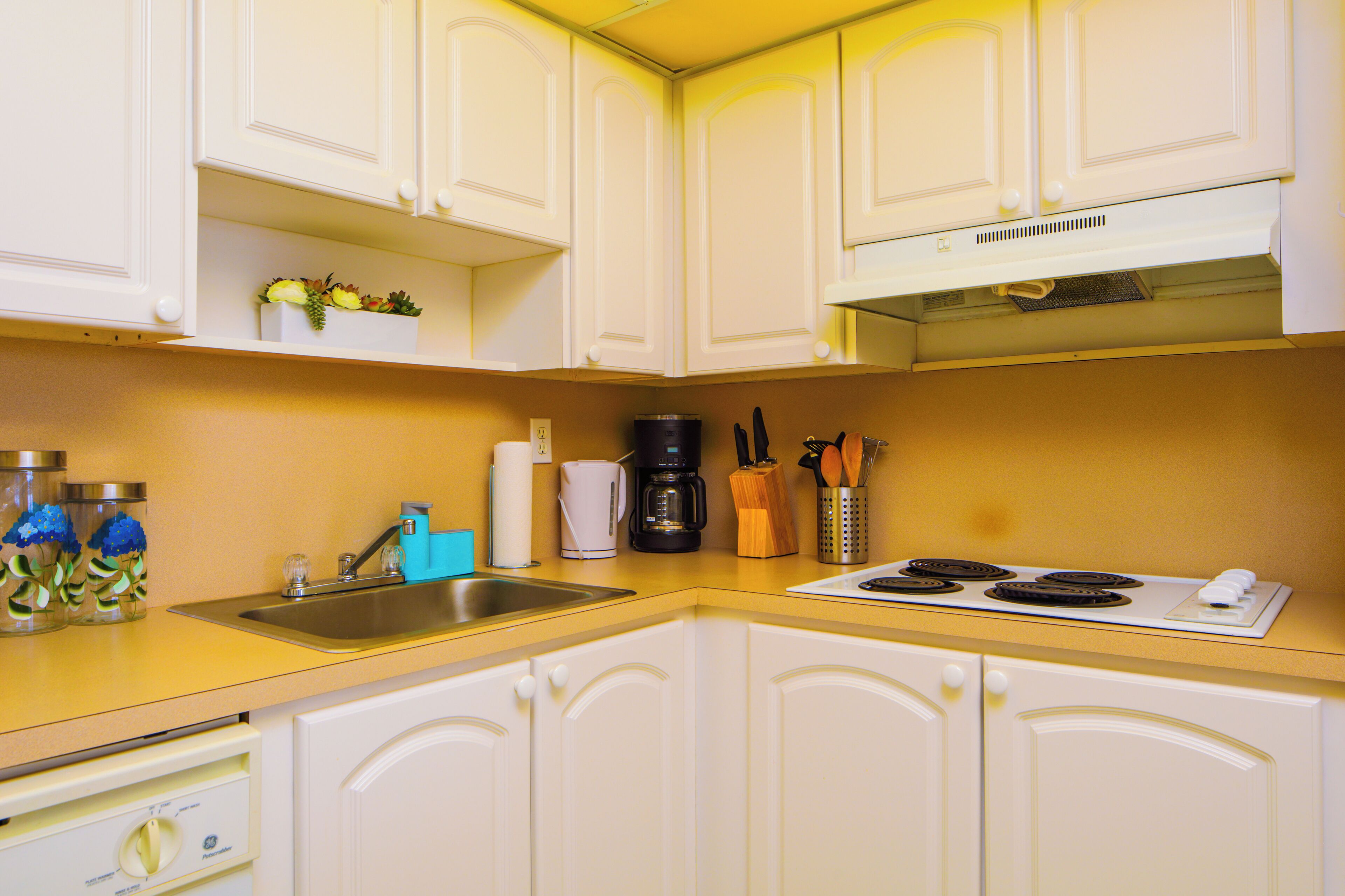 A kitchen with white cabinets, a stainless steel sink, a coffee maker, and a stove.