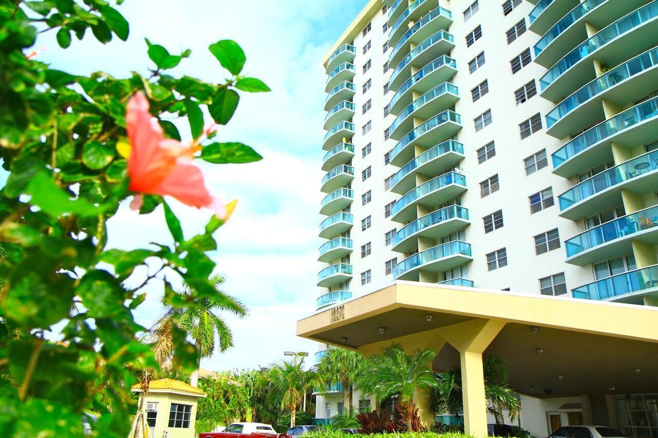 A multi-story hotel with balconies, a covered entrance, and lush greenery.