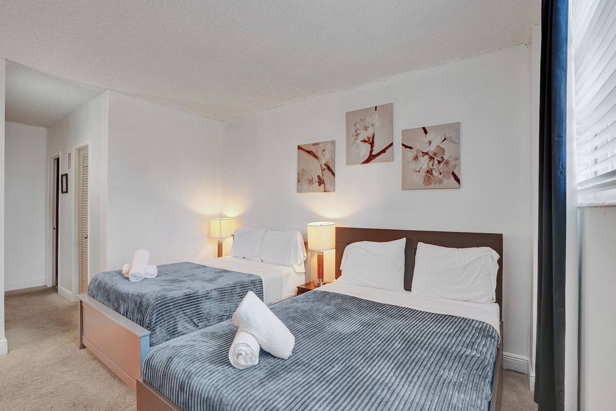 A hotel room with two beds, a door, a lamp, and wall art.