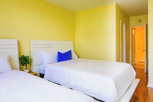 Habitación de hotel con dos camas individuales, una planta en maceta y una puerta que da a otra habitación.