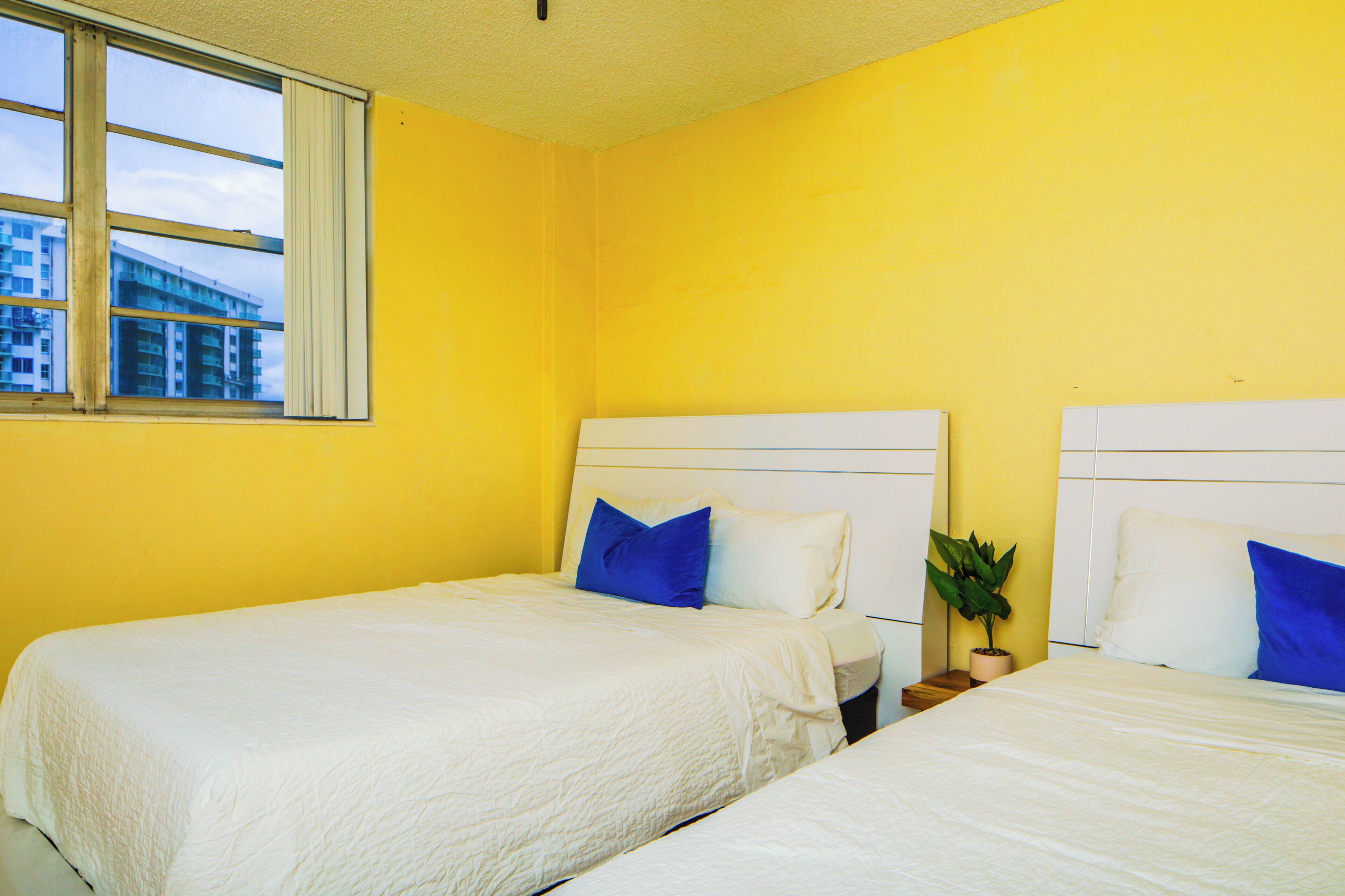 Een hotelkamer met twee bedden, een raam en een potplant.