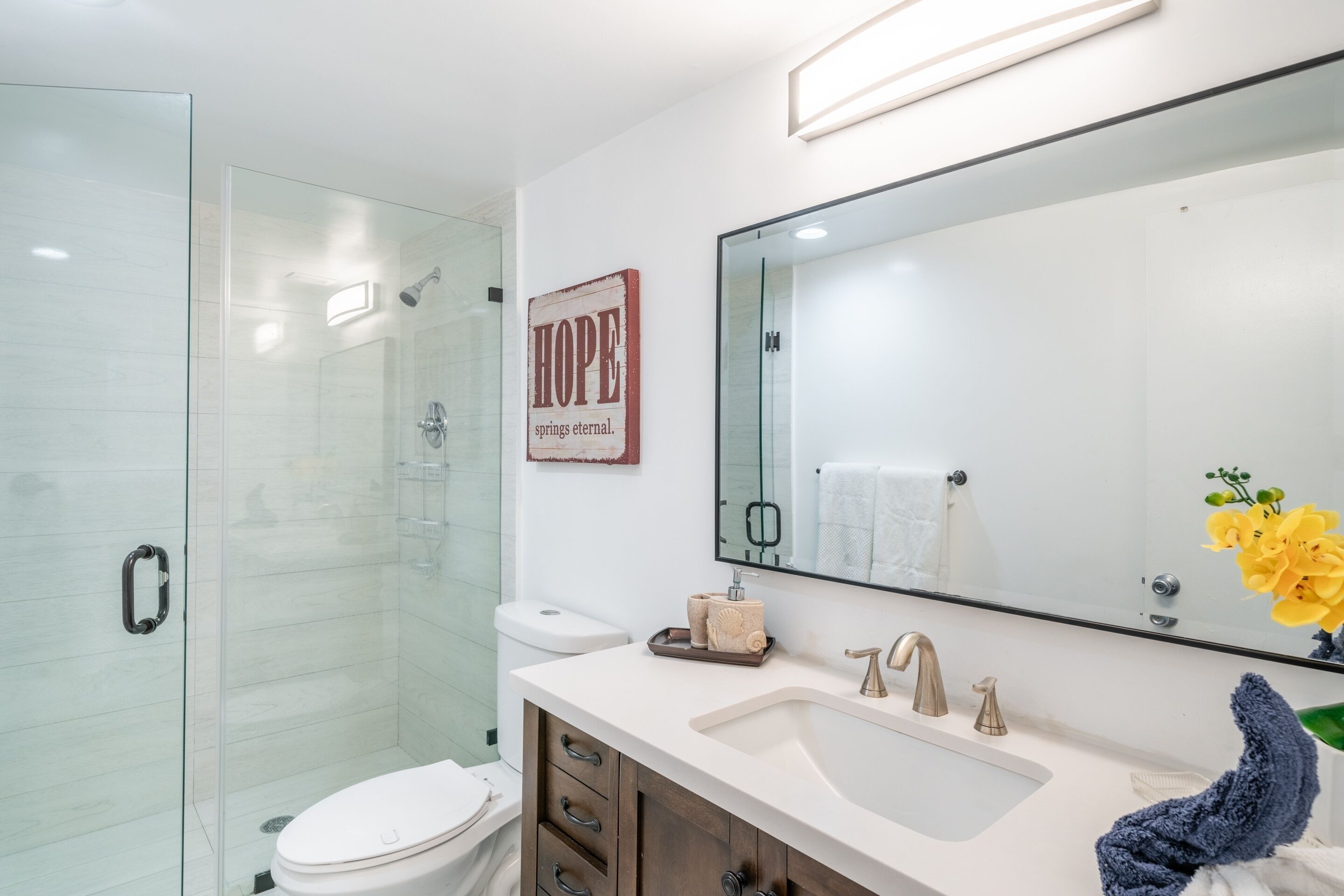 A modern bathroom with a glass shower enclosure, a white sink, and a large mirror.