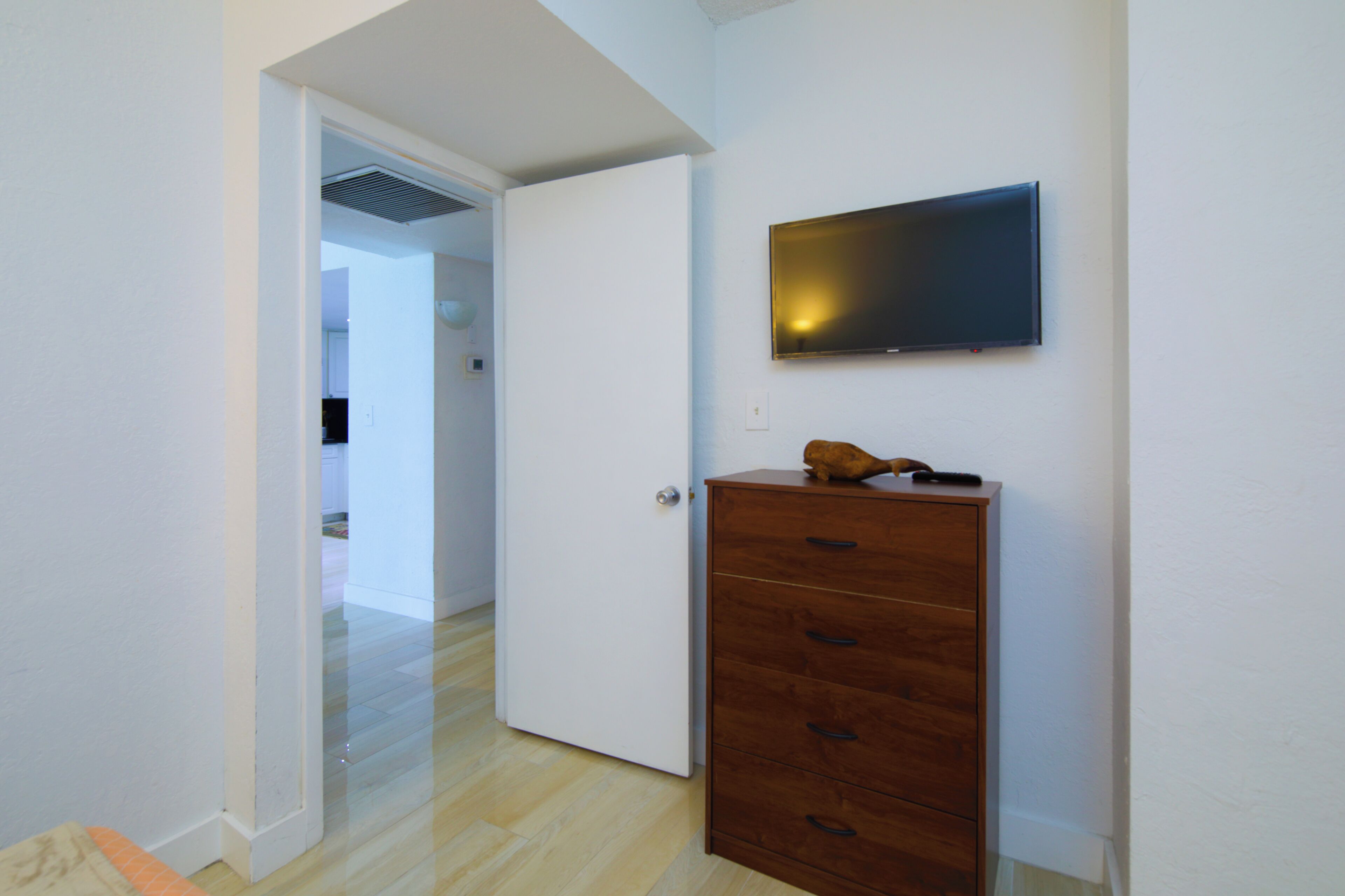 Un pasillo con un aparador de madera, una puerta cerrada y un televisor montado en la pared.