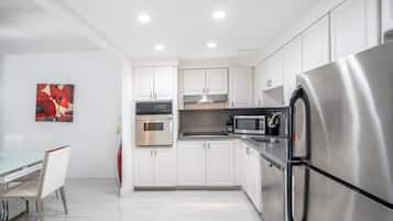 Una cocina moderna con gabinetes blancos, electrodomésticos de acero inoxidable y un comedor con mesa y sillas de vidrio.