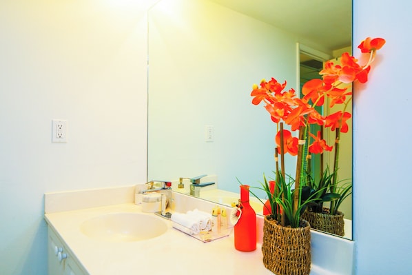 Un baño con un lavamanos blanco, un espejo y un jarrón rojo con flores.