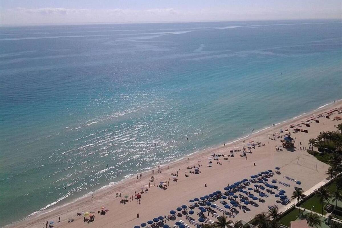 A beach with rows of sun umbrellas and lounge chairs, a sandy shore, and the ocean in the background.