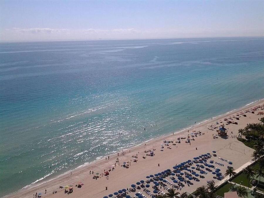 Una playa con hileras de sombrillas y tumbonas, una orilla arenosa y el océano al fondo.