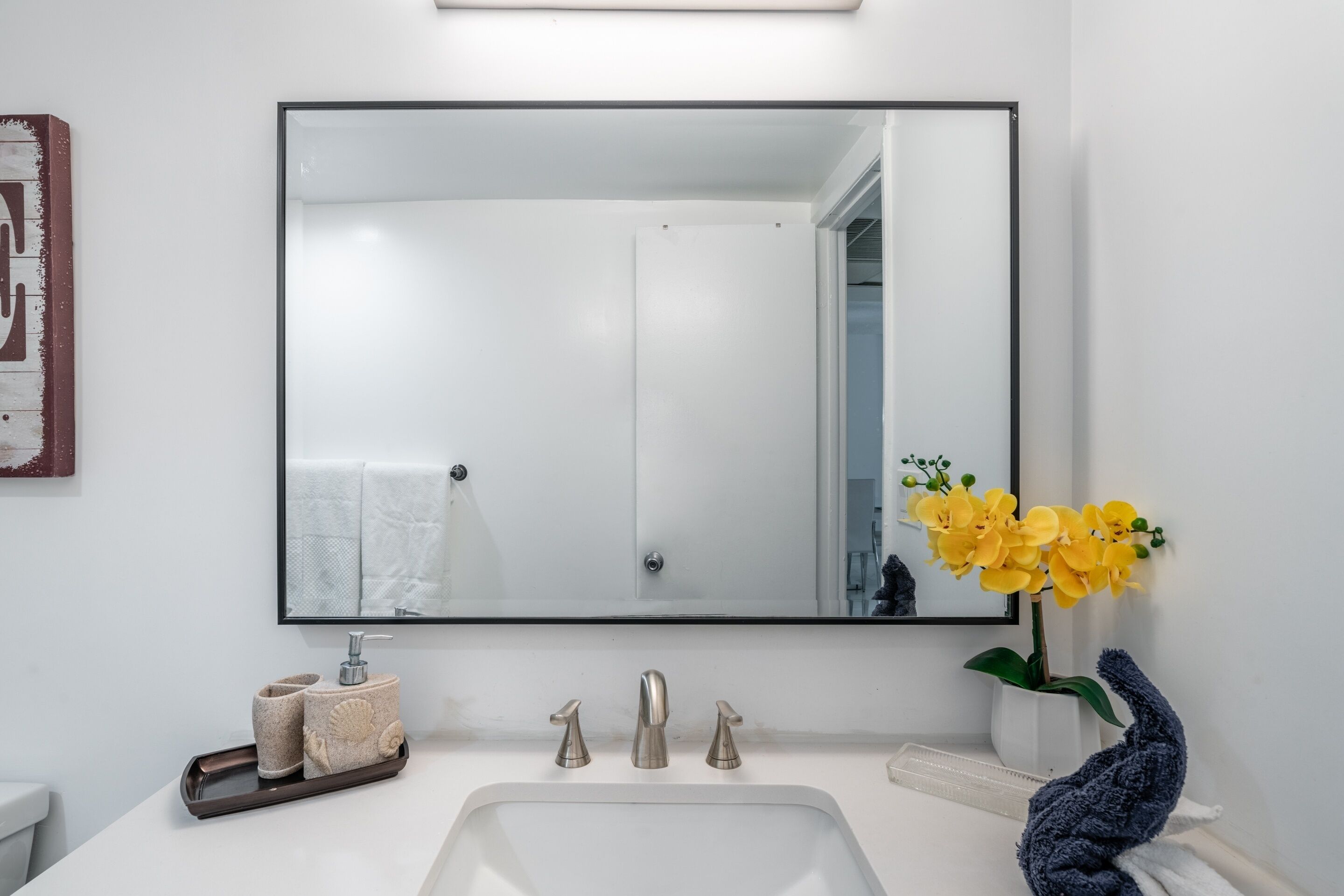 Een badkamer met een wit wastafel, een grote spiegel en een vaas met gele bloemen.