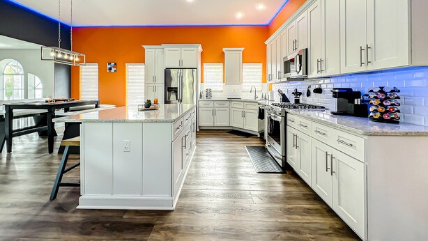 A modern kitchen with white cabinetry, a central island, and a bright orange accent wall.