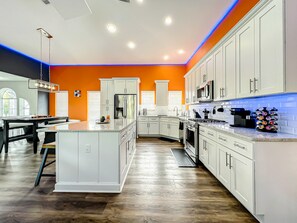 Une cuisine moderne avec des meubles blancs, un îlot central et un mur d’accent d’un orange vif.