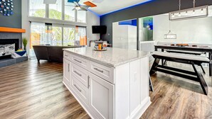 A modern kitchen with a large island, wooden flooring, and a ceiling with geometric light fixtures.