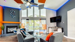 A modern living room with a fireplace, two grey sofas, a ceiling fan, and a large window.
