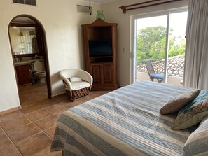 Een slaapkamer met een bed, een stoel, een tv-kast en een balkon met een stoel.