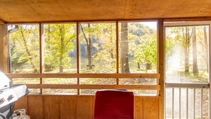 A cabin with a wooden interior, a red chair, and a view of autumn trees through large windows. - Escape to the Shenandoah River and Relax (Luray)