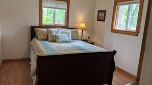 A bedroom with a wooden bed, a patterned bedspread, and two windows with blinds. - Escape to the Shenandoah River and Relax (Luray)