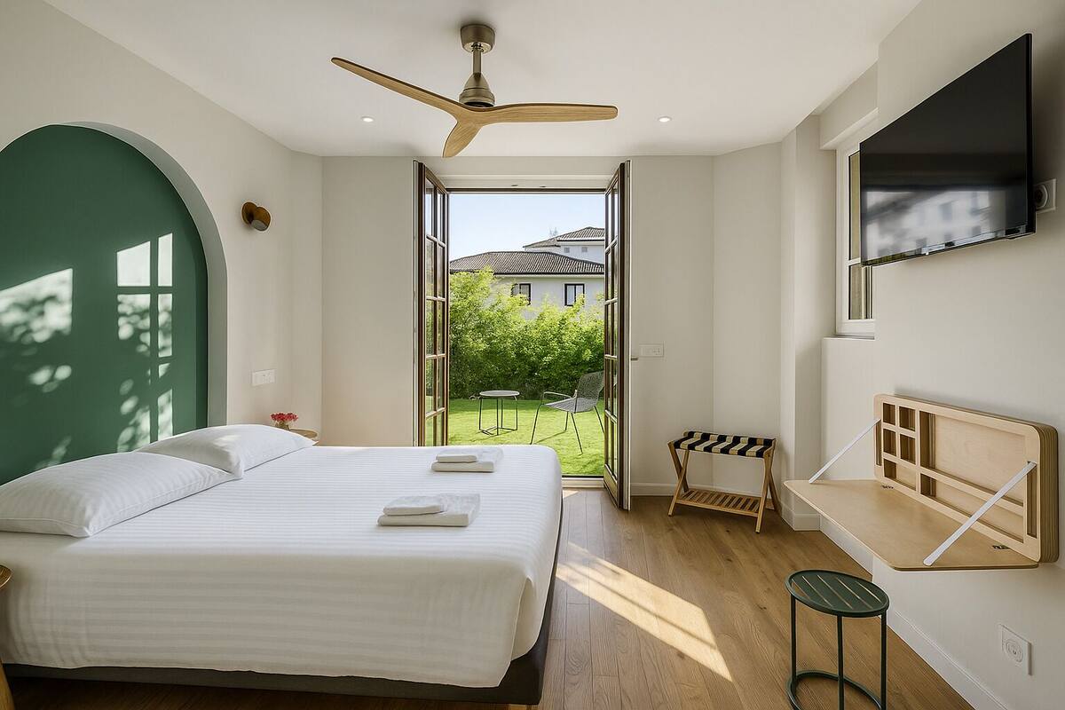 A bedroom with a bed, a ceiling fan, a TV mounted on the wall, and a view of a garden through an open door.