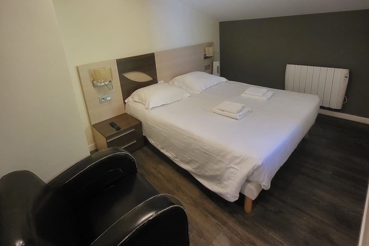 A modern bedroom with a large bed, a massage chair, a bedside table, and a wall-mounted heater.