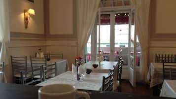 Un comedor con mesas y sillas, una ventana con cortinas, y vista a la calle.