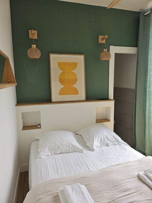 A neatly made bed with white linens, a framed abstract artwork above it, and two wall-mounted lamps. - Hotel Bellevue (Hendaye)