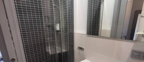 Un baño moderno con ducha envuelta en vidrio, un lavamanos blanco y un espejo sobre él.