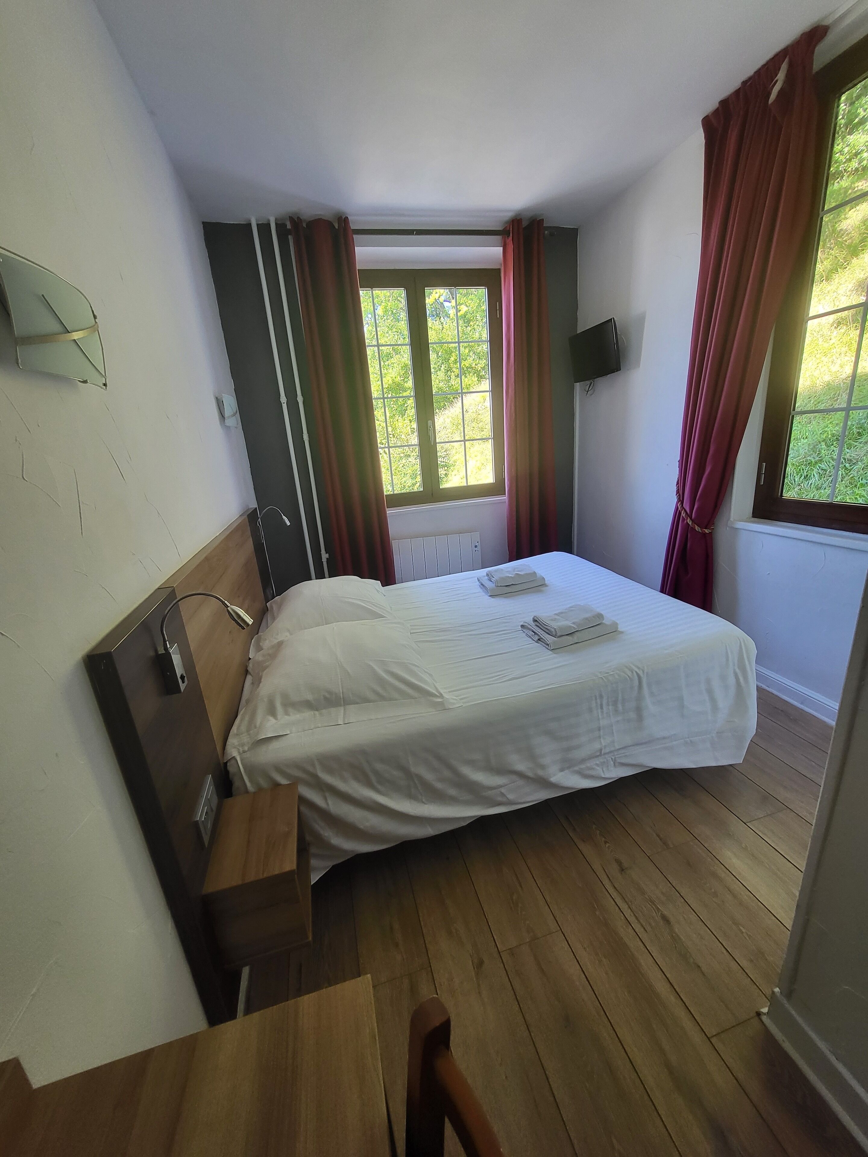 Un dormitorio pequeño y ordenado con una cama individual, un escritorio de madera y una ventana con cortinas.