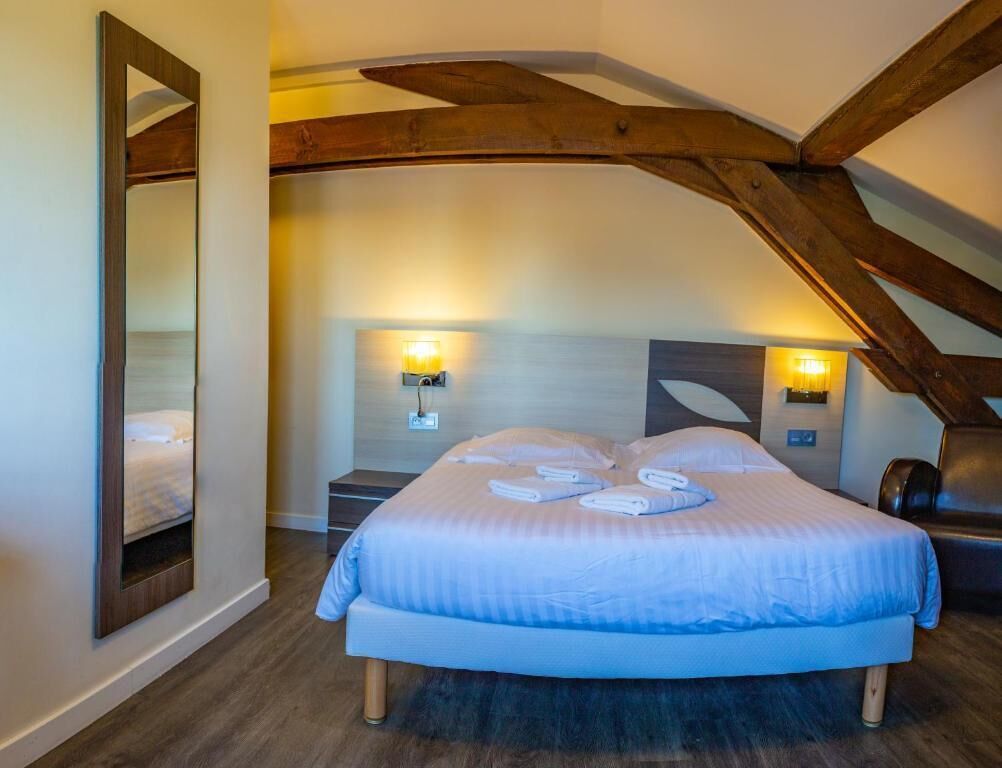 Un dormitorio con una cama grande, vigas de madera, dos lámparas de pared y un espejo.