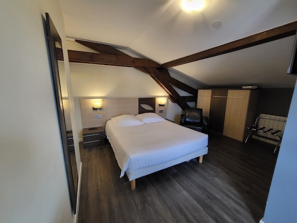 A bedroom with a large bed, wooden beams, a wardrobe, and a chair.