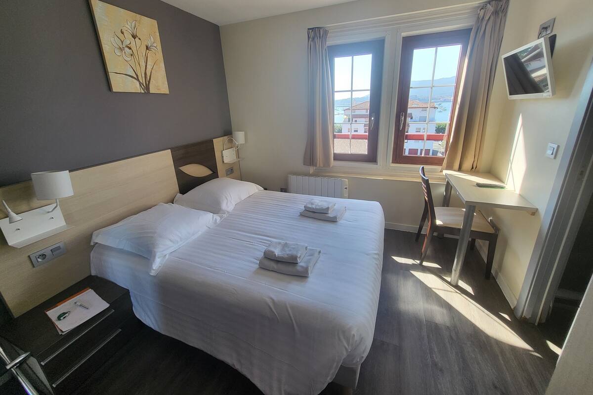 A hotel room with two beds, a desk, a chair, a TV, and a window with curtains.