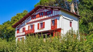 A two-story hotel with a white facade and red accents, surrounded by lush greenery.