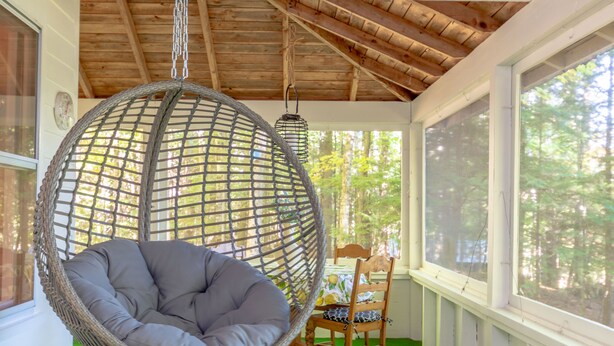 Una habitación con una silla colgante, una mesa de madera con sillas y ventanas amplias que dan a vistas de árboles.