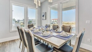 A dining area with a table set for six, large windows, and a view of the beach.