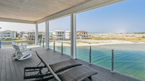A covered outdoor area with a view of the beach and ocean, featuring lounge chairs and a railing.