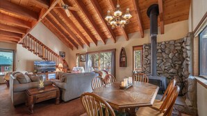 A spacious living area with a wooden ceiling, a stone fireplace, a dining table with chairs, and a staircase leading to another level.