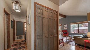 Un couloir avec une armoire en bois, une chaise rouge et un canapé dans un salon donnant sur un bâtiment à l’extérieur.