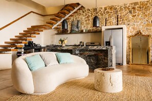 Ein stilvoller Wohnraum mit einer gebogenen Couch, einer Steinwand, einer Küche mit einer Marmorinsel und einer Treppe mit Holzbalken.
