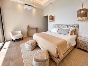 A modern bedroom with a large bed, a chair, a small table, and a decorative wall piece.