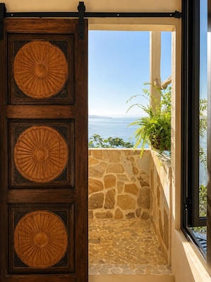 A wooden door with circular patterns, leading to a stone wall and a view of the sea.