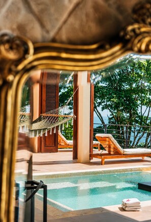 A poolside area with lounge chairs, a hammock, and a view of the sea.
