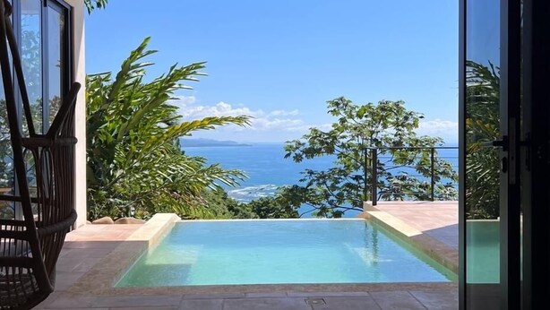 Blick vom Zimmer mit Glastür auf einen Infinity-Pool mit Meerblick.