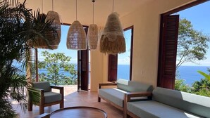 Ein Zimmer mit großem Fenster, einer Couch, einem Sessel, einem kleinen Tisch und Pendelleuchten.