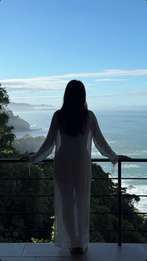 Una persona de pie junto a una ventana con vista al océano.