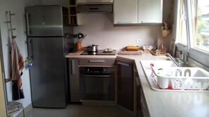 A compact kitchen with a refrigerator, oven, and dishwasher. There is a window providing natural light and a view of the outside.