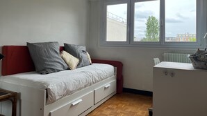 A compact bedroom with a bed, a small desk, and a window with a view of buildings and trees.
