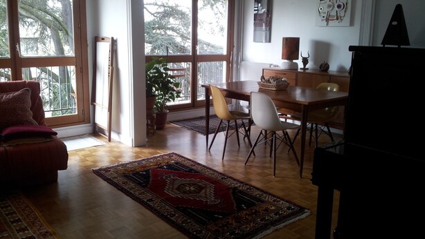 A spacious living room with a large window, a dining area with a wooden table and chairs, and a cozy seating area with a sofa.