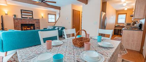 A dining area with a table set for four, a fireplace, and a living room with a blue sofa.